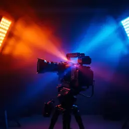 Professional film camera on tripod with orange and blue LED lighting panels creating dramatic bi-color setup in studio