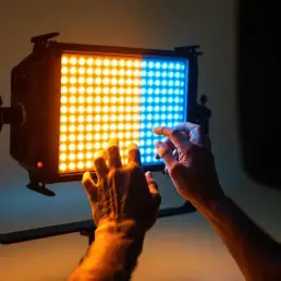 Professional LED light panel with warm golden and cool blue light gradient as photographer adjusts color temperature dial