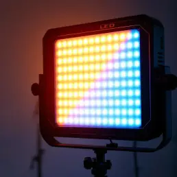 Professional LED light panel on studio stand casting warm golden and cool blue dual-tone lighting in photographer workspace.
