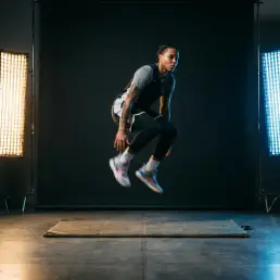 Athlete mid-leap in photography studio lit by warm-amber and cool-blue LED panels, motion blur on sneakers, low-angle shot on polished concrete floor.