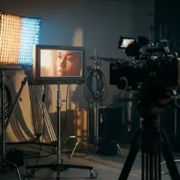 Professional video monitor displaying accurate skin tones on a film set, lit by a bi-colour LED panel casting warm amber and cool daylight.