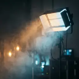 Bi-colour LED fixture projecting warm amber and cool daylight beams through volumetric haze on a cinematic set.