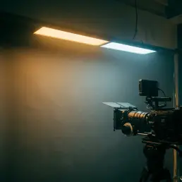 Bi-colour LED panel casting warm amber and cool daylight zones on a cinema camera, dramatic chiaroscuro with teal shadows and golden highlights.