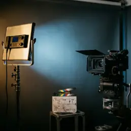 Bi-colour LED panel casting warm amber and cool daylight beams on a grey studio wall beside a cinema camera and production slate.