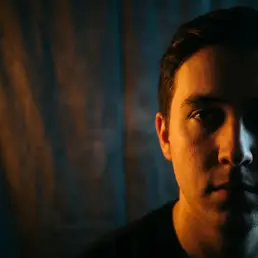 Cinematographer's face split between warm amber and cool daylight from a bi-colour LED panel against a shadowed studio backdrop.