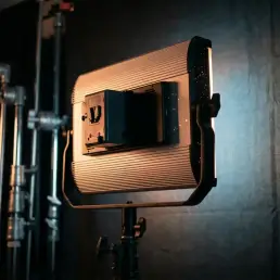 Bi-colour LED panel light on a studio stand powered by a V-mount battery, emitting warm tungsten and cool daylight tones against a dark cinematic backdrop.