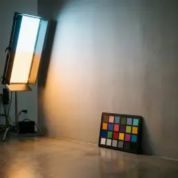 Bi-colour LED panel casting warm amber and cool 5600K daylight beams blending on a grey studio wall, with a colour checker chart below.