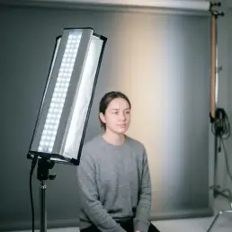 Bi-colour LED studio light casting soft, diffused cool-white glow across a minimalist grey seamless backdrop with warm-to-cool gradient.