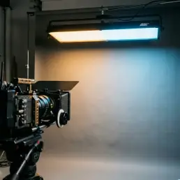 Cinema LED light panel casting warm amber and cool daylight blue pools on a gray studio backdrop, cinema camera visible in foreground.