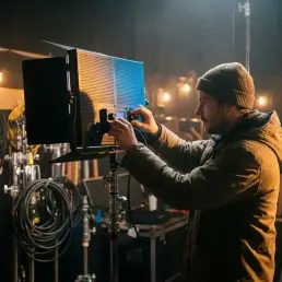 Cinematographer adjusting a bi-colour LED panel on a film set, warm tungsten bulbs and cool daylight tones blending in the cinematic background.