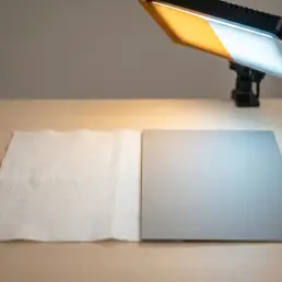 White fabric swatch and grey card lit by warm-to-cool bi-colour LED, revealing texture shifts and soft shadows in studio close-up.