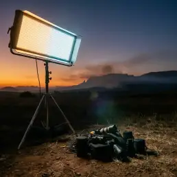LED bi-colour light panel on tripod outdoors during golden-hour sunset, casting warm amber and cool daylight tones across a dramatic dusk landscape.
