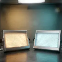 Two professional LED lighting panels on a dark studio surface, one emitting warm amber and the other cool daylight blue light.