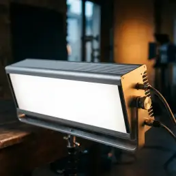 Professional LED panel light with aluminum body emitting crisp white light against a dark studio background with warm golden side-fill.