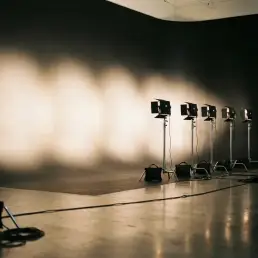 Premium LED panel lights on studio stands casting uniform warm white beams across a dark gray cyclorama, reflecting on polished concrete floor.