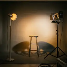 Two studio LED lights facing an empty portrait stool, casting overlapping warm and cool pools on a grey seamless backdrop.